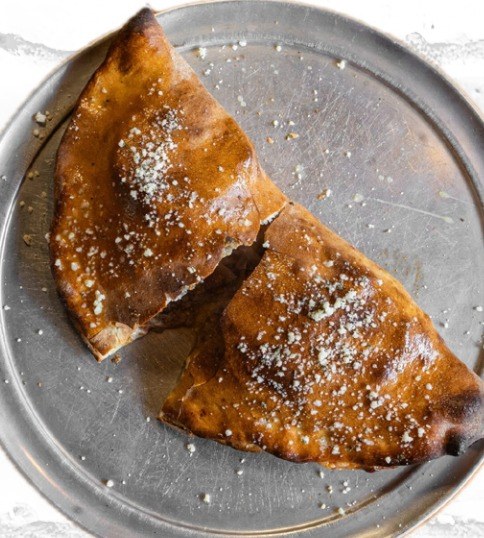 A folded, baked dough pocket on a metal pizza pan, browned on top and dusted with cheese.
