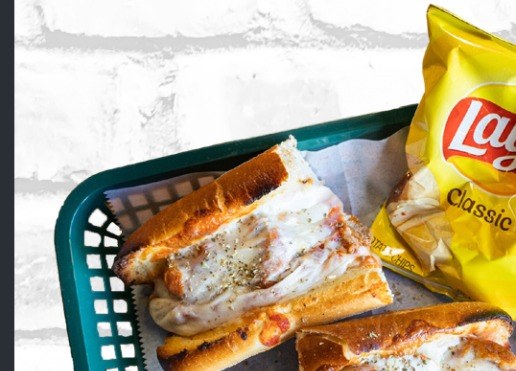Two halves of a hot sub in a green plastic basket with a bag of Lay’s chips beside them.